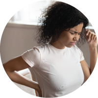 Young African American woman sitting at table with laptop at home, suffering from pain.