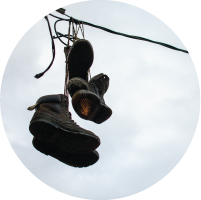 Worn boots hanging from a wire against a cloudy sky.